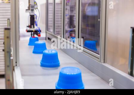 Pots bleus sur le tapis de la machine de moulage par injection plastique avec bras robotisé Banque D'Images