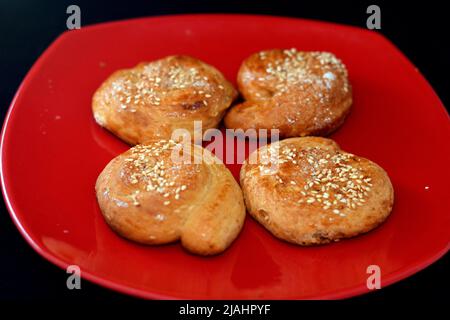 Cuisine orientale arabique égyptienne de petits gâteaux arrondis couverts de sésame et de sucre, desserts de fête Eid El Fitr et bonbons du Ramadan sur un plat rouge en céramique Banque D'Images