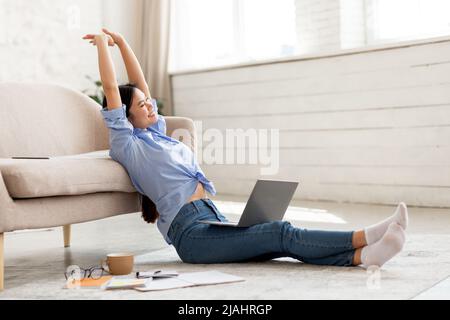 Joyeuse femme chinoise qui s'étire tout en utilisant un ordinateur portable Banque D'Images