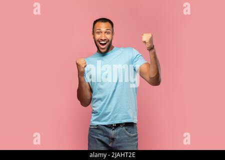 Un jeune homme noir surjoyé criant dans l'excitation, en faisant un geste OUI avec les deux mains sur fond rose studio Banque D'Images