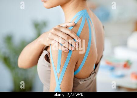 Gros plan de la jeune femme avec du ruban bleu de physio sur l'épaule soulageant la douleur musculaire dans la thérapie de réadaptation, l'espace de copie Banque D'Images