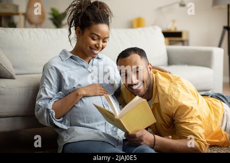 Couple afro-américain lisant le livre s'attendant à bébé à la maison Banque D'Images