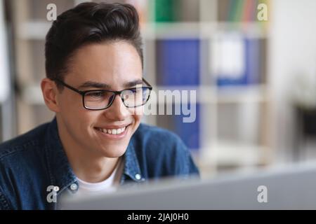 Gros plan de Smiling Young Man en lunettes travailler avec un ordinateur portable au bureau Banque D'Images