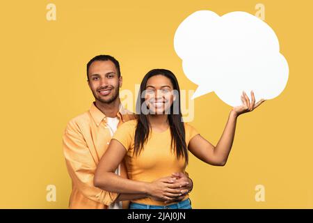 Portrait d'un jeune couple afro-américain tenant une bulle de discours vide avec maquette pour votre dessin sur fond jaune Banque D'Images