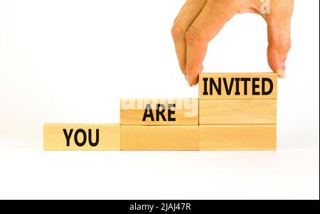 Vous êtes invité. Concept mots vous êtes invités sur des blocs de bois. Main d'homme d'affaires. Magnifique table blanche fond blanc. Et vous Banque D'Images