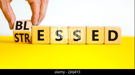 Symbole béni ou stressé. L'homme d'affaires tourne des cubes en bois et change le mot concept souligné à Blessed. Magnifique table jaune fond blanc. Banque D'Images