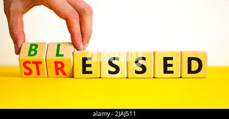 Symbole béni ou stressé. L'homme d'affaires tourne des cubes en bois et change le mot concept souligné à Blessed. Magnifique table jaune fond blanc. Banque D'Images