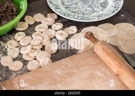 Préparation des boulettes. Garniture de viande dans une tasse, boulettes de pâte et une planche à rollPIN. Banque D'Images