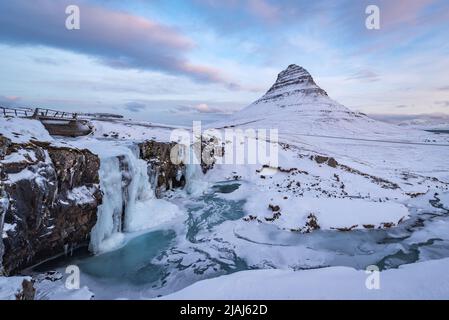 La chute d'eau gelée de Kirkjufellfoss en Islande en hiver, couverte de glace et de neige avec la montagne Kirkjufell en arrière-plan Banque D'Images