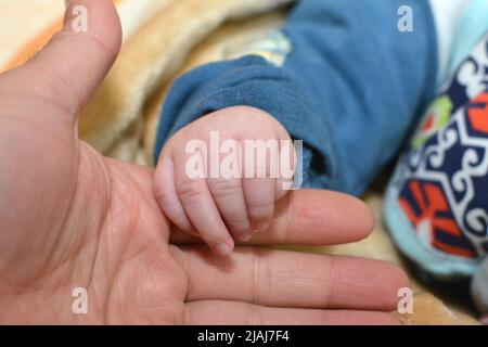 La main d'un nouveau-né dans la main d'un papa sur un fond flou, gros plan nouveau-né tenant la main de son père, amour de la santé familiale et médicale Banque D'Images