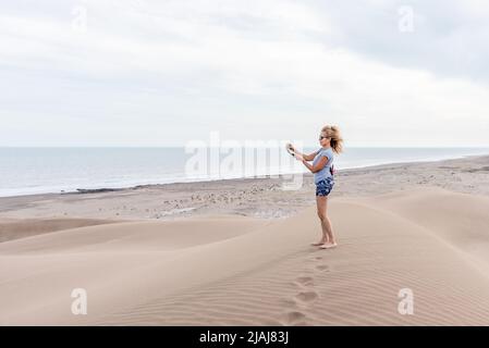 Photo verticale d'une femme avec des lunettes de soleil à l'aide d'un trépied portable pour prendre un selfie dans une dune Banque D'Images