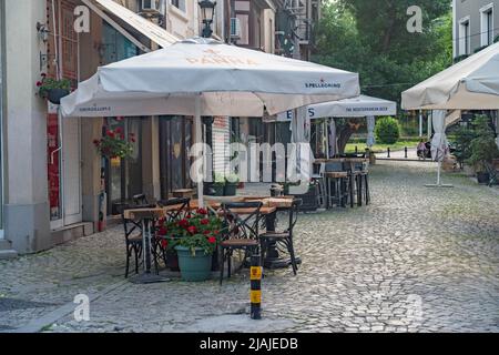 Plovdiv, Bulgarie - 22.05.2022: Café de rue pavée avec des tables et des chaises vides rassemblés et parasols ouverts le matin à Plovdiv, Bulgari Banque D'Images