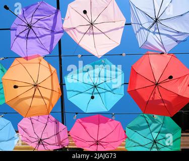 Parapluies suspendus à des câbles créant un effet de plafond; rangées de parasols décoratifs de couleur pastel en translucide dans le ciel bleu vif rempli de soleil Banque D'Images