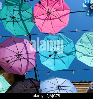 Parapluies suspendus à des câbles créant un effet de plafond; rangées de parasols décoratifs de couleur pastel en translucide dans le ciel bleu vif rempli de soleil Banque D'Images