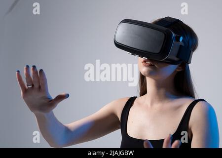 Surprise heureuse fille brune en t-shirt noir se faisant découvrir les lunettes VR de réalité virtuelle et explorant de nouveaux mondes cybernétiques. Banque D'Images