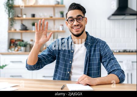 Charmant indien ou arabe, assis à la maison, parler avec webcam, avoir un appel vidéo ou une conversation avec un client ou un collègue, le mentor enregistrer cours de formation, salue l'interlocuteur, souriant amical Banque D'Images
