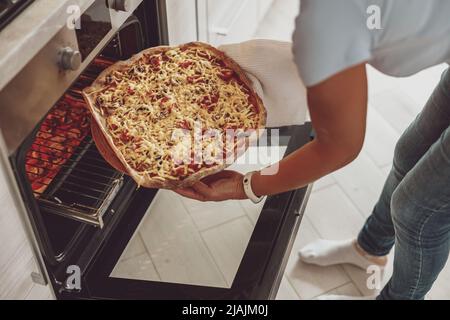 Une femme met de la pizza sur la plaque de cuisson dans le four ouvert Banque D'Images