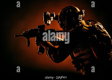 Un soldat des opérations spéciales portant un dispositif de vision nocturne, visant un fusil d'assaut à canon court dans l'obscurité. Banque D'Images
