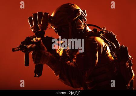 Un soldat des opérations spéciales portant un dispositif de vision nocturne, visant un fusil d'assaut à canon court dans l'obscurité. Banque D'Images