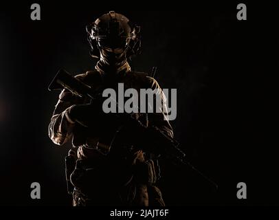 Portrait en studio à clé d'un soldat d'élite des forces spéciales de l'Armée debout avec une carabine d'assaut dans l'obscurité. Banque D'Images