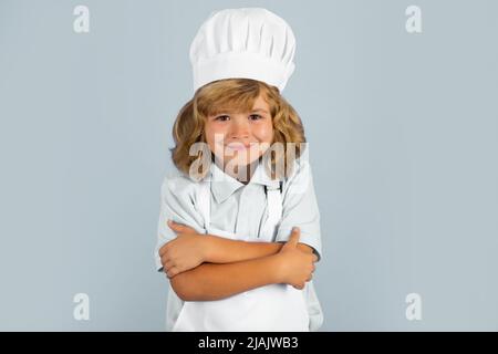 Portrait de chef enfant isolé sur bleu. Drôle petit chef cuisinier enfant portant uniforme chapeau de cuisinier et tablier aliments cuits dans la cuisine. Banque D'Images