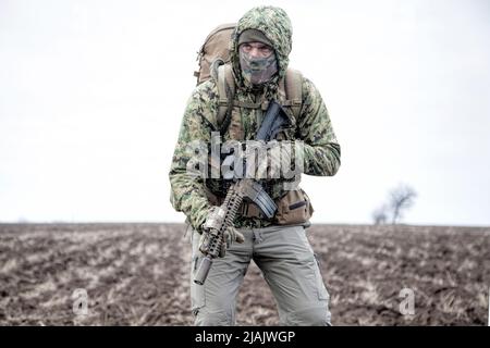 Militaire mercenaire portant une veste de camouflage à capuche et un sac à dos, marchant sur un terrain boueux. Banque D'Images