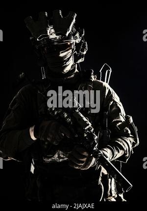 Portrait d'un soldat des forces spéciales armé d'une sous-machine, debout dans l'obscurité. Banque D'Images