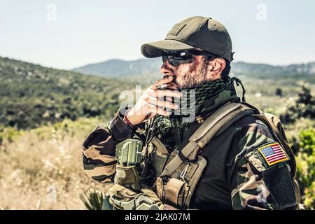 Soldat en pleine tenue fume une cigarette dans la région de montagne. Banque D'Images