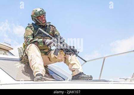Navy Seals chasseur assis sur l'arc d'un bateau de vitesse avec le fusil de service en main. Banque D'Images