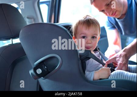 Père plaçant son petit garçon dans le siège de voiture Banque D'Images