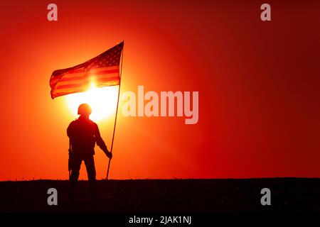 Silhouette d'un soldat américain portant le drapeau américain contre un ciel de coucher de soleil. Banque D'Images