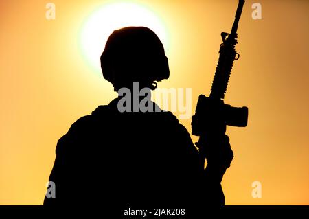 Silhouette d'un soldat debout avec un fusil d'assaut à la main contre un ciel de coucher de soleil. Banque D'Images