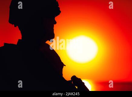 Silhouette d'un soldat patrouilant le littoral au coucher du soleil. Banque D'Images