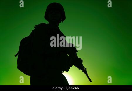 Silhouette de rifleman portant un sac à dos tactique et une carabine de service, avec fond de ciel de coucher de soleil. Banque D'Images