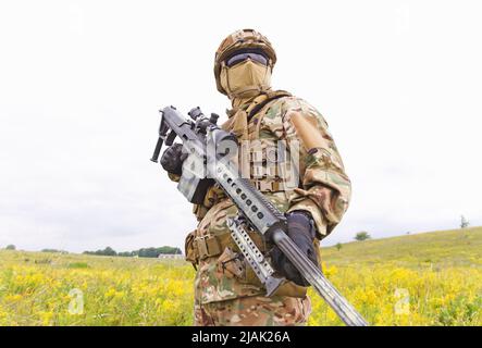 Soldat armé des forces spéciales avec fusil de sniper debout sur le terrain. Banque D'Images