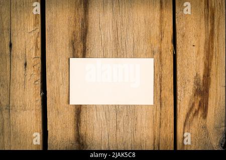 Une carte de visite vierge sur fond en bois. Un rectangle en papier blanc se trouve sur les anciens panneaux fissurés. Mise au point sélective. Banque D'Images