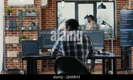 Codage par programmation sur ordinateur portable assis au bureau avec écrans d'ordinateur analysant le code dans l'agence logicielle. Développeur de logiciels compilant des algorithmes avec des programateurs de cloud fonctionnant en arrière-plan. Banque D'Images