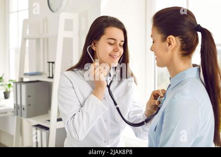 Une jeune infirmière amicale écoute le cœur de la femme et souffle à travers le stéthoscope sur sa poitrine. Banque D'Images
