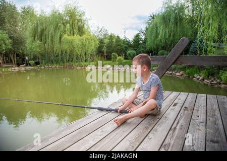 Un garçon triste est assis sur le lac et attrape du poisson. Journée internationale des enfants Banque D'Images