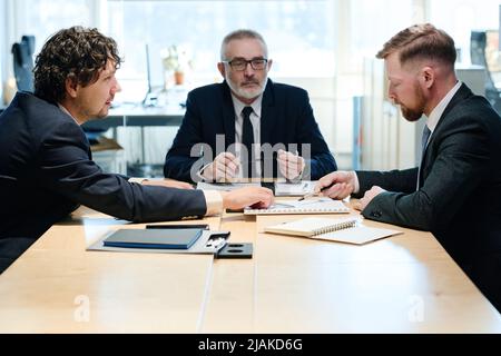 Groupe de managers en costume discutant du rapport d'affaires à table pendant le travail d'équipe lors de la réunion Banque D'Images