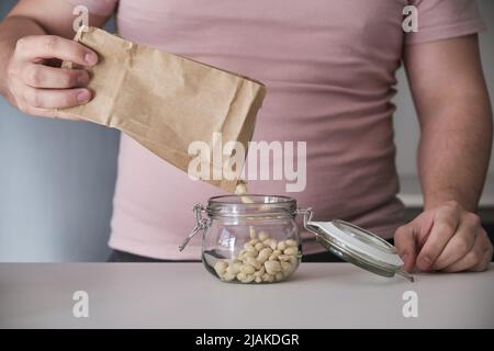 latins méconnaissables remplissant un pot avec des arachides pelées dans un sac en papier. Banque D'Images