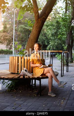 Style de ville. Une fille est assise sur un banc et lit un livre Banque D'Images