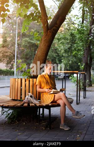 Style de ville. Une fille est assise sur un banc et lit un livre Banque D'Images