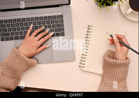 Coup de tête, une femme blogueuse travaillant dans son espace de travail, utilisant un ordinateur portable pour rechercher des idées et prendre une liste sur le journal. Banque D'Images