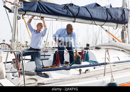 Deux jeunes hommes en chemises bleues arrange le yacht privé de voile dans le port maritime Banque D'Images