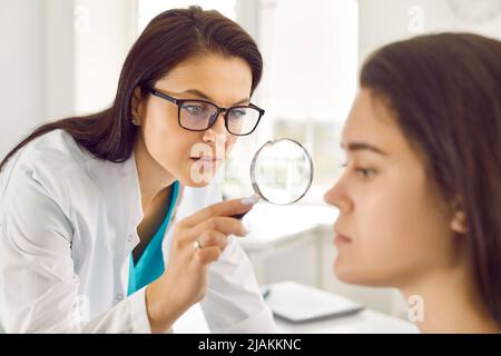 Dermatologue utilise la loupe pour examiner la peau problématique sur le visage de la jeune femme Banque D'Images