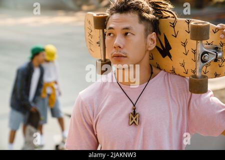 Un garçon asiatique tient un skateboard tout en passant du temps au skate Park en plein air Banque D'Images