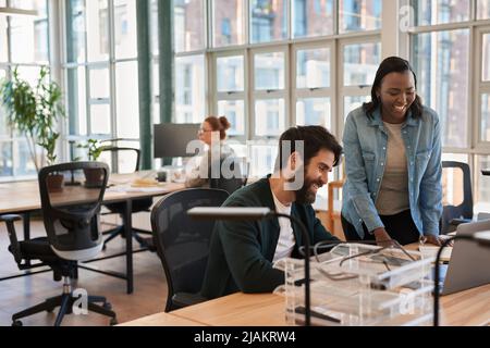 Deux jeunes hommes d'affaires divers souriant tout en travaillant ensemble sur un ordinateur portable Banque D'Images