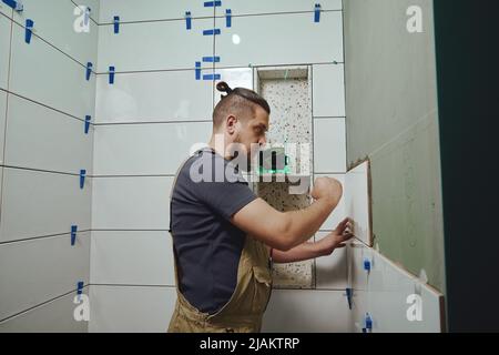 Carreleur posant des carreaux de céramique sur le mur dans la salle de bains Banque D'Images