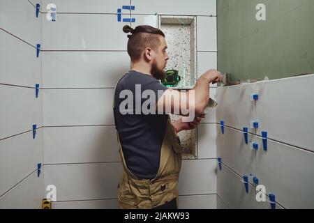 Réparateur appliquant de l'adhésif pour carreaux avec une truelle sur le mur de la salle de bains Banque D'Images